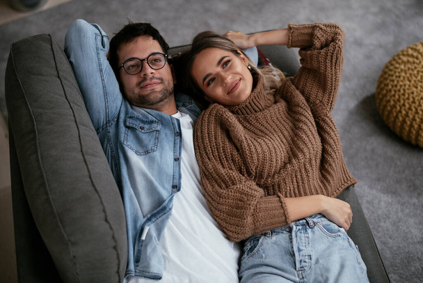 Young loving couple relaxing on sofa together. Happy couple enjoying at home. - Foto, imagen