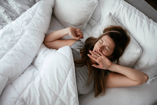 Woman stretching in bed after wake up. Beautiful girl enjoying morning light. - Foto, Imagem