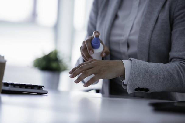 businesswoman in grey suit disinfecting hands in the office - Fotografie, Obrázek