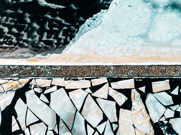 Abstract winter ijs achtergrond textuur van gebarsten bevroren rivier water oppervlak en drijvend ijs stukken, stenen pier van boven - Foto, afbeelding