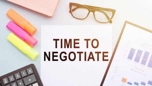 The text "TIME TO NEGOTIATE" on office desk with calculator, markers, glasses and financial charts. - Photo, Image