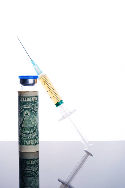 Vial dose of COVID-19 vaccine with syringe wrapped dollar bill against white background, global vaccination and money abuse concept - Photo, Image
