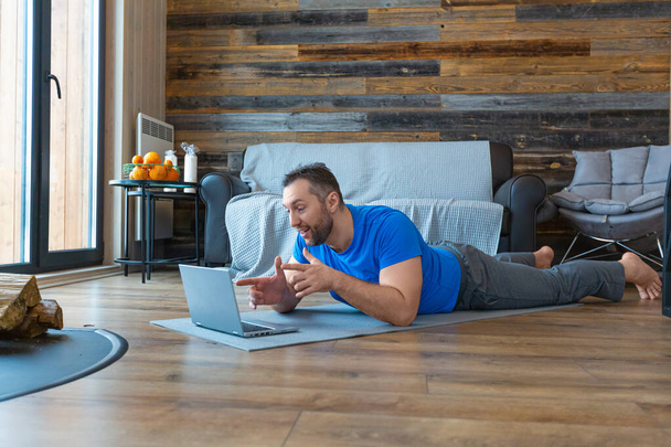 Ein Mann bei einem Online-Videoanruf. Er liegt auf dem Boden vor einem Laptop-Monitor. - Foto, Bild