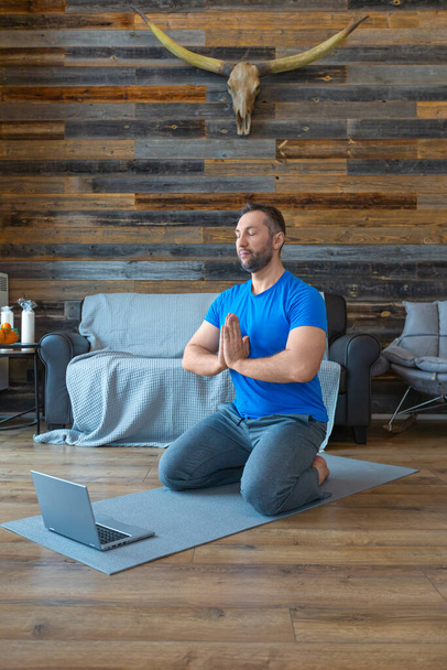Mężczyzna medytuje w domu online przed monitorem laptopa. - Zdjęcie, obraz