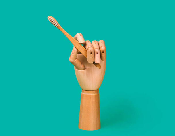 Wooden mannequin hand holding bamboo toothbrush. Dental care concept. Isolated on blue background. - Foto, immagini