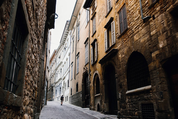 Podróże solo. Samotny podróżnik spaceruje wąską uliczką po domach starego europejskiego miasta. Turystyka w Europie. - Zdjęcie, obraz