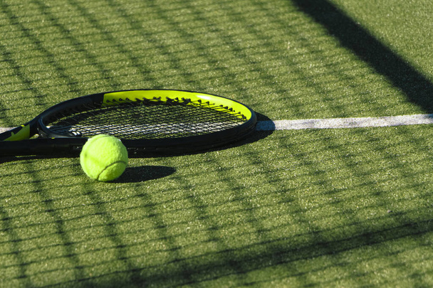 Μπάλα τένις και ρακέτα στο έδαφος ενός πράσινου γηπέδου τένις - Φωτογραφία, εικόνα