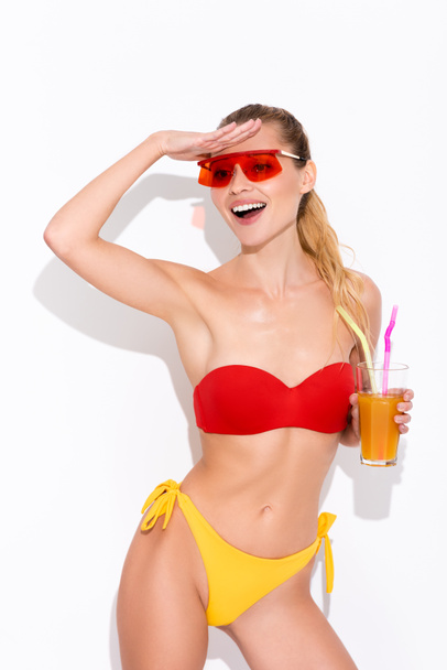 excited woman in swimsuit looking away while holding refreshing cocktail on white - Foto, Imagem