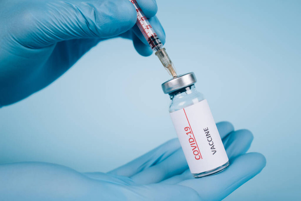 Médico ou cientista injetando a dose do frasco para injetáveis da vacina COVID-19 com seringa contra fundo azul com espaço de cópia - coronavírus de prevenção, conceito de vacinação global, foco seletivo - Foto, Imagem