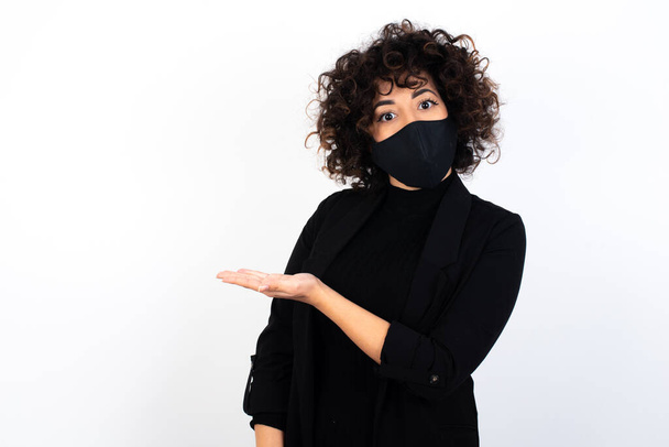 caucasian woman wearing medical mask says: wow how exciting it is, has amazed expression, shows something on blank space with palm. Advertisement concept. - Photo, Image