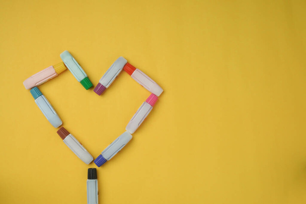 Watercolor tubes, placed in the shape of a heart, on a yellow background, in the view from above, with gaps. - Photo, Image