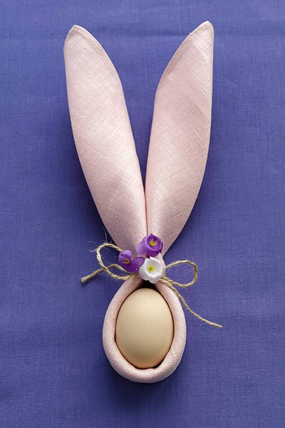 Decoratieve konijnenoren met ei op paars katoenen tafelkleed om Pasen te vieren, doe-het-zelf, plat gelegd - Foto, afbeelding