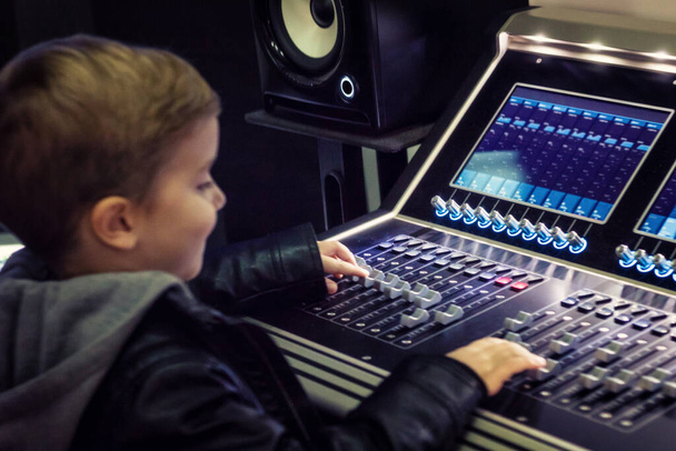 Kleiner Junge schneidet Musik am elektronischen Mischpult im Tonstudio.  - Foto, Bild