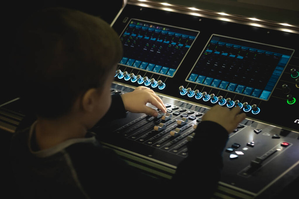 Little DJ editing music and adjusting volume at audio mixer panel in recording studio. - Photo, Image
