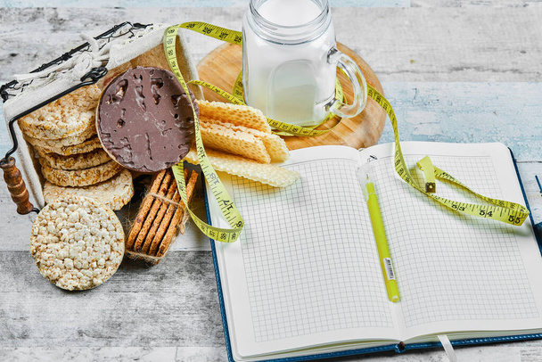 Mand met koekjes en een pot melk op een houten tafel met notebook - Foto, afbeelding
