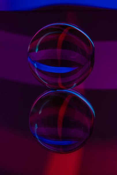 Skleněná křišťálová koule na zrcadlovém povrchu s modrým a fialovým vzorem světelné malířské fraktály na černém pozadí - Fotografie, Obrázek