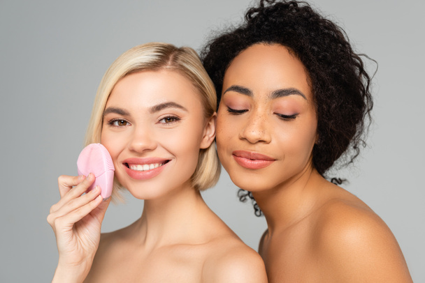 Multiethnic women with naked shoulders holding silicone brush isolated on grey  - Фото, зображення