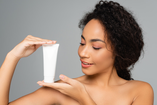 Smiling african american woman positing with tube of cleansing foam isolated on grey  - Foto, immagini