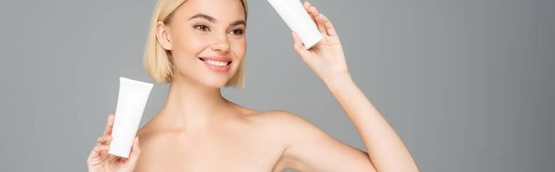 Young woman with clean skin holding tubes with cleansing foam isolated on grey, banner  - Fotó, kép