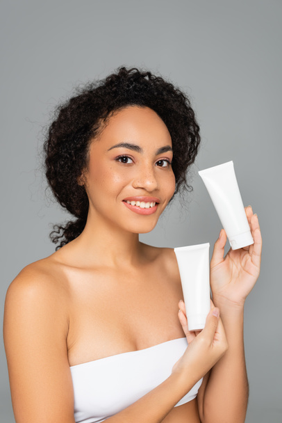 Young african american woman holding tubes with cleansing foam isolated on grey  - Foto, afbeelding