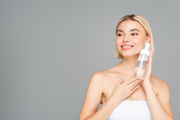 Cheerful blonde woman holding cleansing foam isolated on grey with copy space  - Foto, immagini