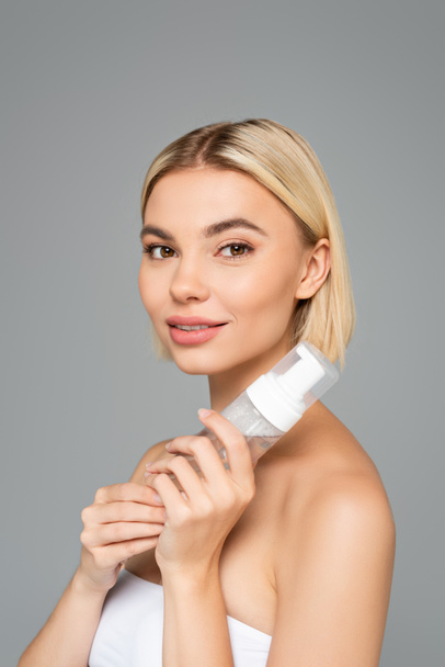 Young woman with clean skin looking at camera while holding cleansing foam isolated on grey  - Photo, Image