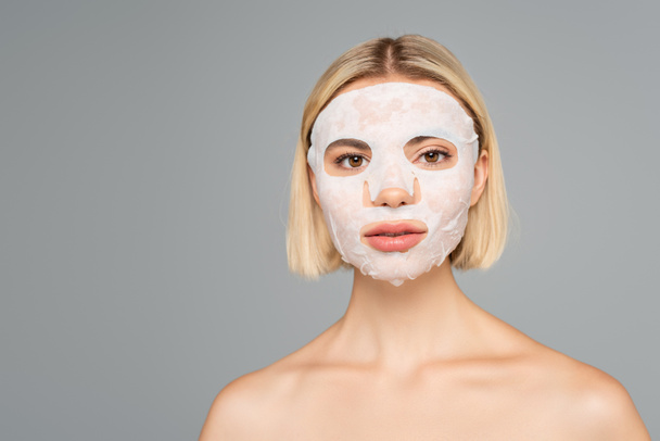 Young woman with naked shoulders and sheet mask on face isolated on grey  - Photo, Image