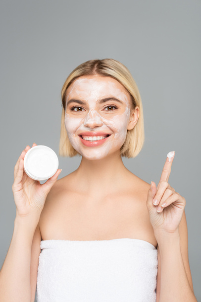 Blonde woman with facial mask holding cosmetic cream isolated on grey  - Foto, Imagem