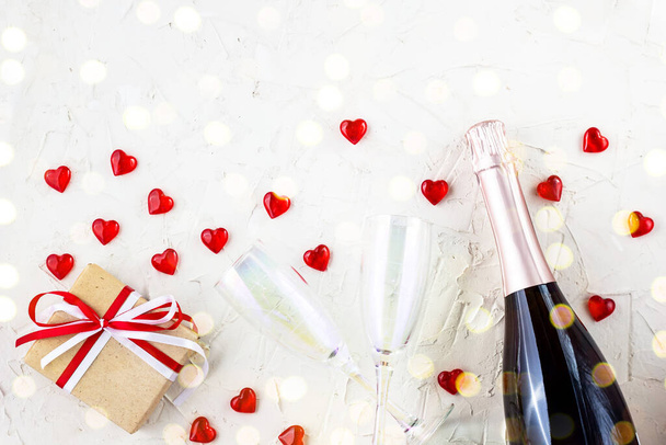 Biglietto di San Valentino con bicchieri di champagne e bottiglia, cuore e regalo su sfondo bianco. Vista dall'alto, copiare spazio. colorato con bokeh - Foto, immagini
