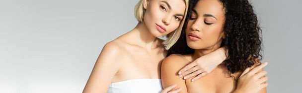 Blonde woman embracing african american woman on grey background, banner  - Zdjęcie, obraz