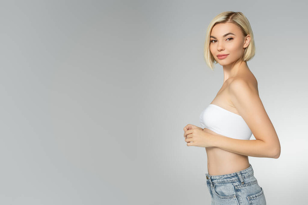 Blonde woman in white top looking at camera isolated on grey  - Photo, Image