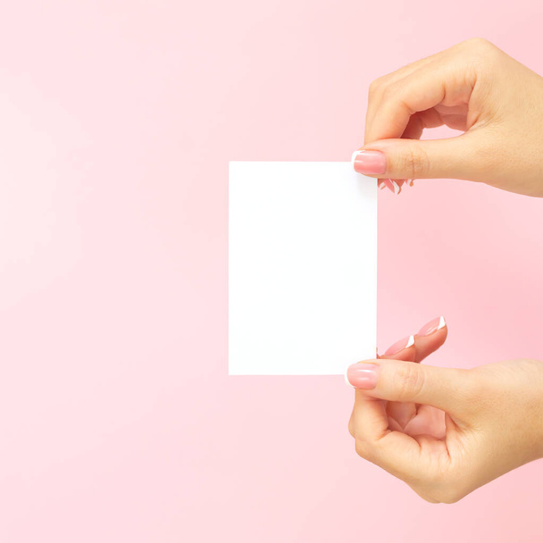 Γυναίκα χέρια κρατώντας κενό λευκό επαγγελματική κάρτα, έκπτωση ή φυλλάδιο σε ροζ φόντο με αντίγραφο χώρο. Πρότυπο για το σχεδιασμό σας - Φωτογραφία, εικόνα