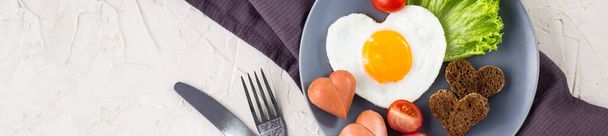 Banner des Valentinstagsfrühstücks mit herzförmigen Spiegeleiern, serviert auf grauem Teller. flache Lage, Draufsicht - Foto, Bild