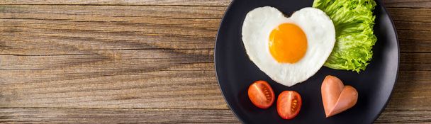 banner of Fried eggs in the shape of a heart with sausages, herbs and tomatoes. Breakfast for your loved ones on Valentine's day on wooden background. Top view with copy space - Φωτογραφία, εικόνα