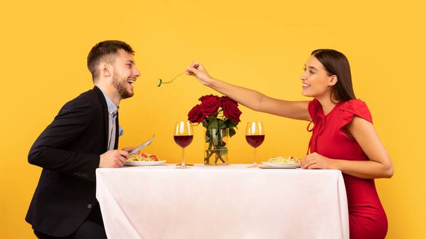 Loving Couple Feeding Each Other During Date On Yellow Background - Photo, Image