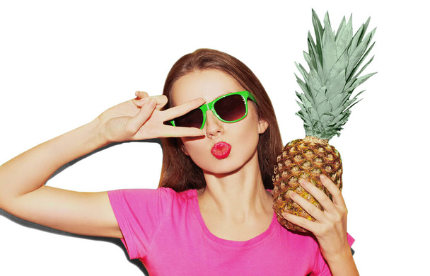 Portrait close up of young woman with pineapple blowing lips wearing a sunglasses isolated on a blue background - Фото, зображення