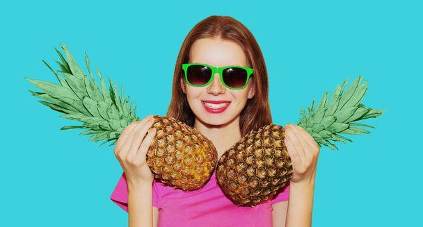 Portrait of cheerful smiling young woman model with pineapple wearing a sunglasses isolated on a blue background - Foto, afbeelding