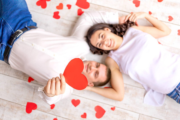 valentine's day, a couple in love lies among the hearts on the floor hugging and holding a large red heart - Foto, Imagem