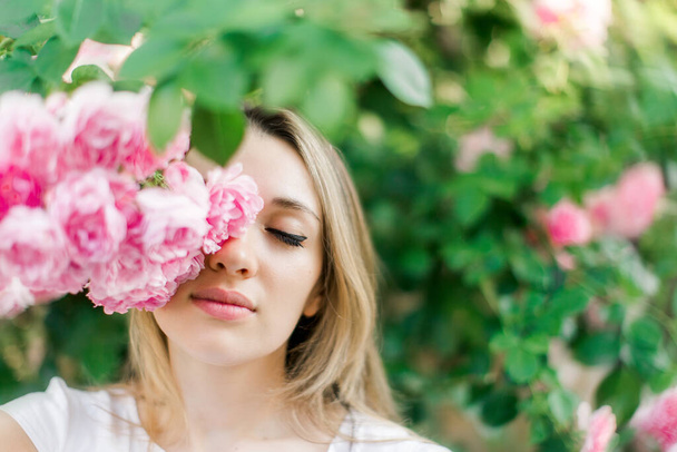 Blond lovely girl with blooming roses.Outdoors portrait,spring time. - Zdjęcie, obraz