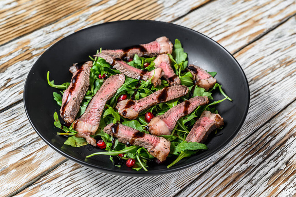 Steak de bœuf grillé tranché avec salade de feuilles de roquette. Fond en bois blanc. Vue du dessus. - Photo, image