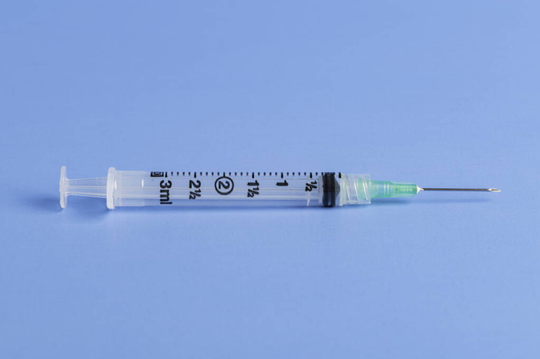 A close-up shot with selective focus of an hygienic single-use plastic disposable medicine injection syringe set on a plain blue background. - Fotó, kép