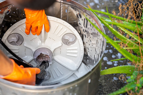 Un uomo che indossava guanti di gomma arancione spruzzava la base della lavatrice pulita con un tubo ad alta pressione. - Foto, immagini