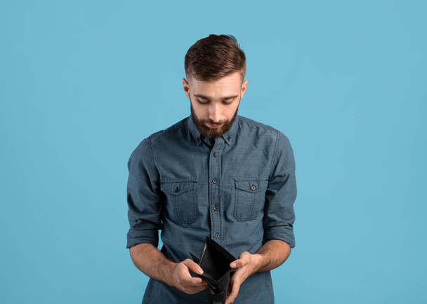Poverty and unemployment. Desperate young man showing empty wallet with no money over blue studio background - Foto, Bild