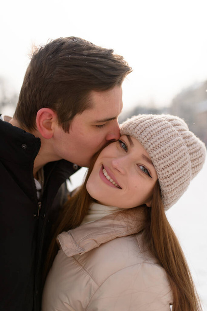 Молодая пара целуется под огромной сосной в городе, покрытом белым снегом - Фото, изображение