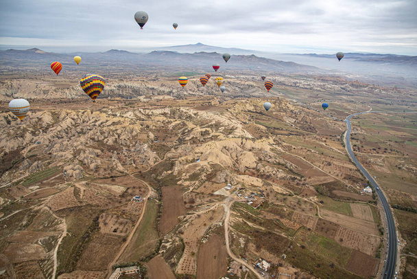 Πολύχρωμα αερόστατα θερμού αέρα αιωρούνται πάνω από ορεινό τοπίο με δρόμο στην Καππαδοκία της Τουρκίας - Φωτογραφία, εικόνα