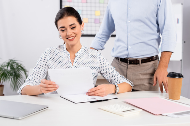 cheerful businesswoman looking at document near coworker standing at desk - Foto, immagini