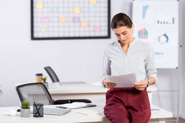 Geschäftsfrau stützt sich auf Schreibtisch und hält Dokumente im Büro - Foto, Bild