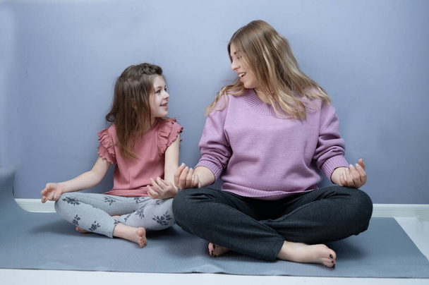 Caucasian little girl with mother pregnant make yoga at home together - Zdjęcie, obraz