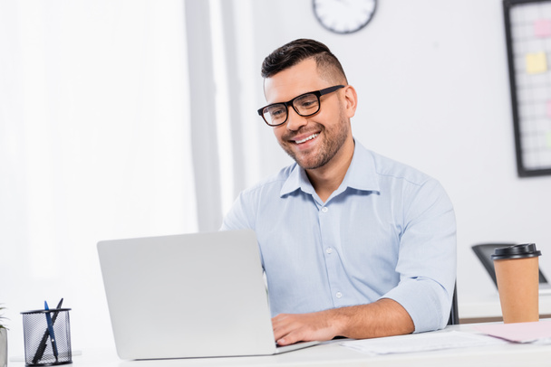 счастливый бизнесмен в очках с помощью ноутбука в офисе - Фото, изображение