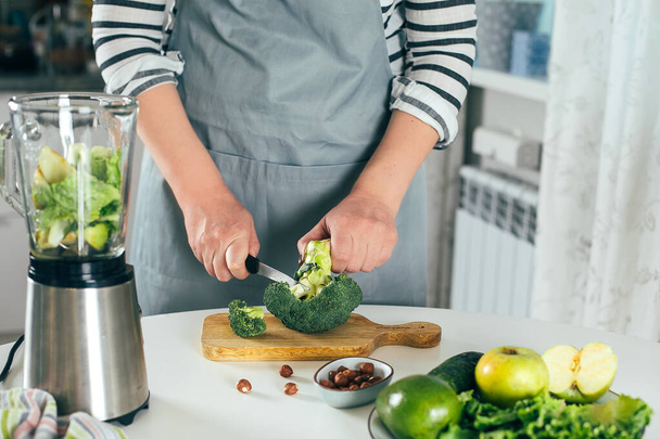Woman cuts broccoli, makes healthy green smoothie. Vegetarian, clean eating lifestyle concept. - Φωτογραφία, εικόνα